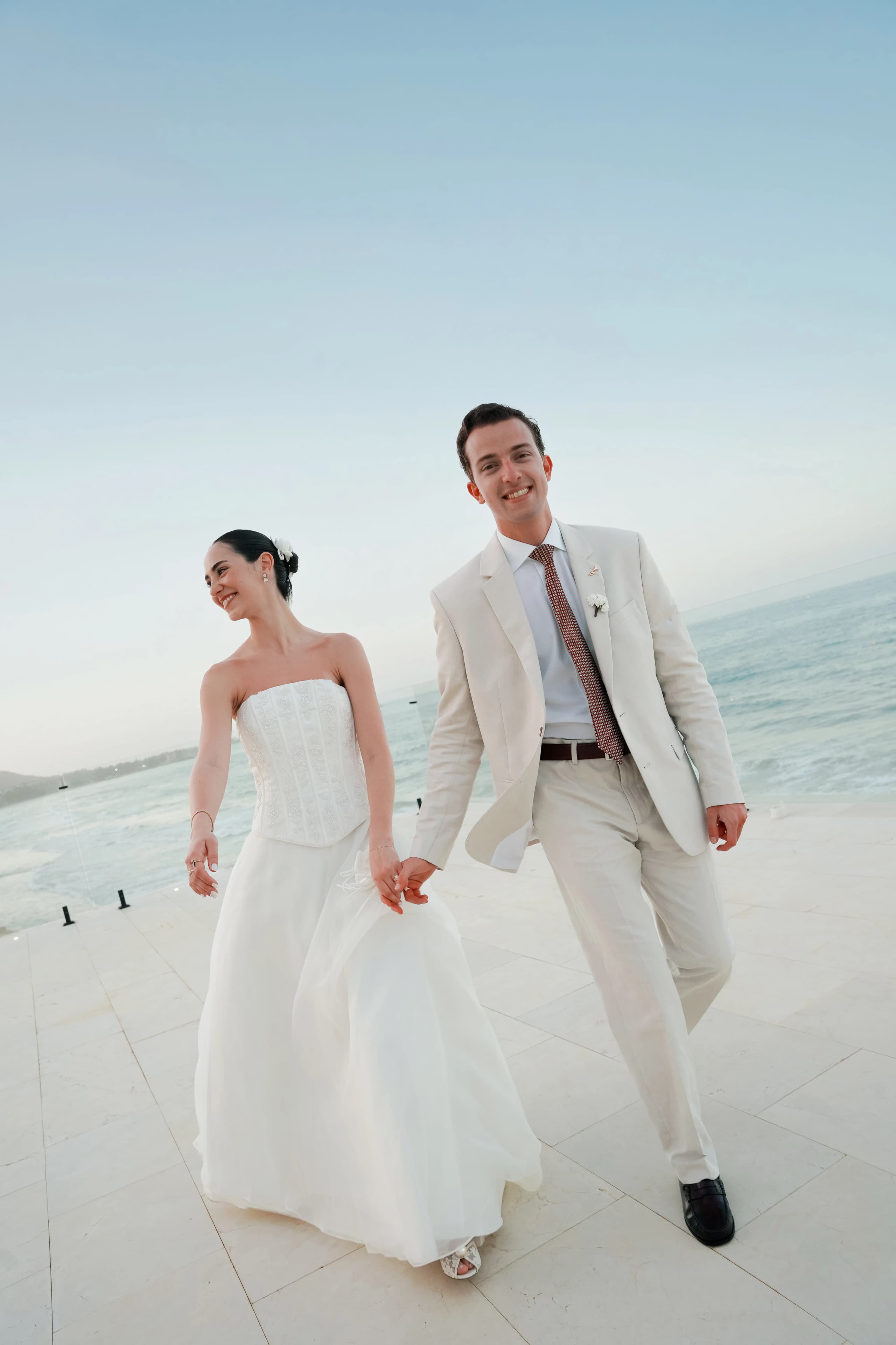 Novios caminando tomados de la mano y sonriendo frente al mar con luz del Caribe, boda editorial en la Isla de Margarita por Andreagsfoto